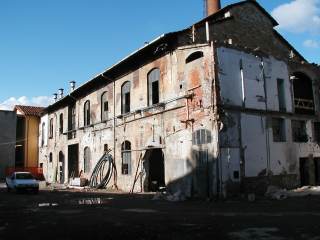 L\'edificio della vecchia fabbrica durante i lavori, con le pareti senza intonaco, le tubature in vista e le finestre con i vetri rotti.